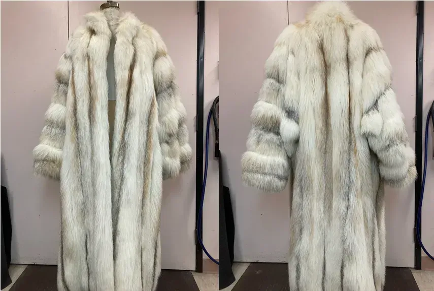 A full-length white fox coat photographed front and back against the Edwards-Lowell workroom wall, available to rent